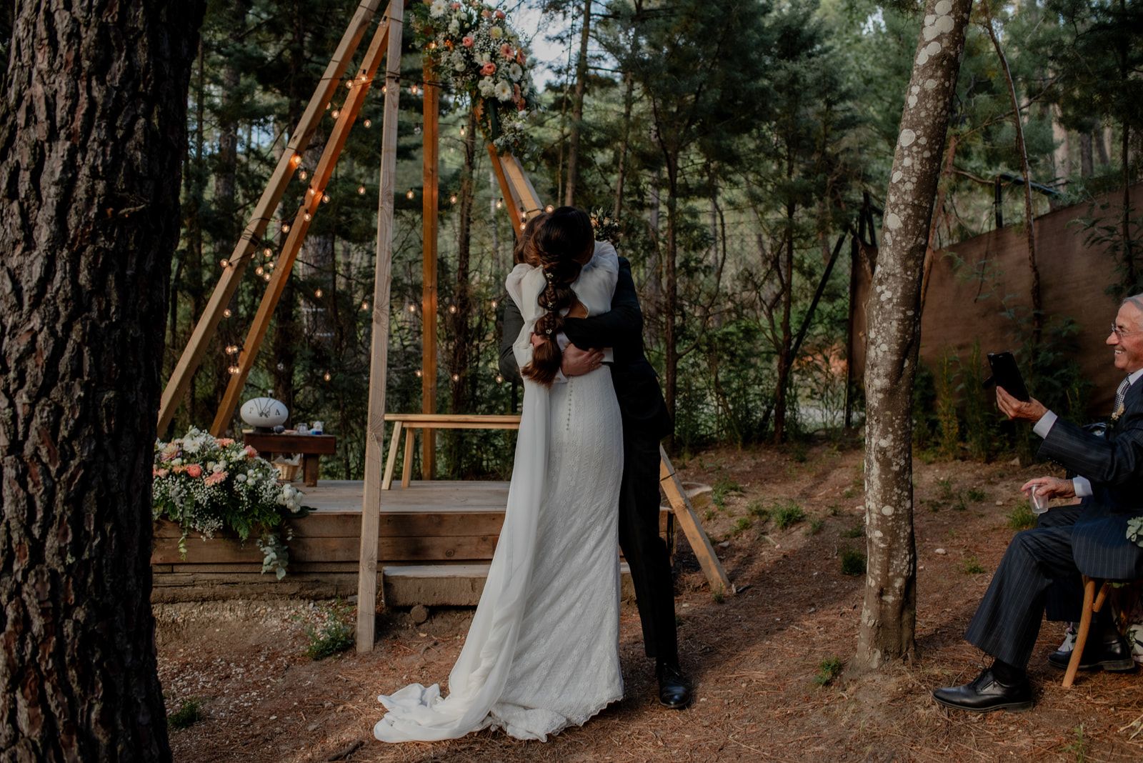 Novios abrazados frente al altar de madera en el claro del bosque
