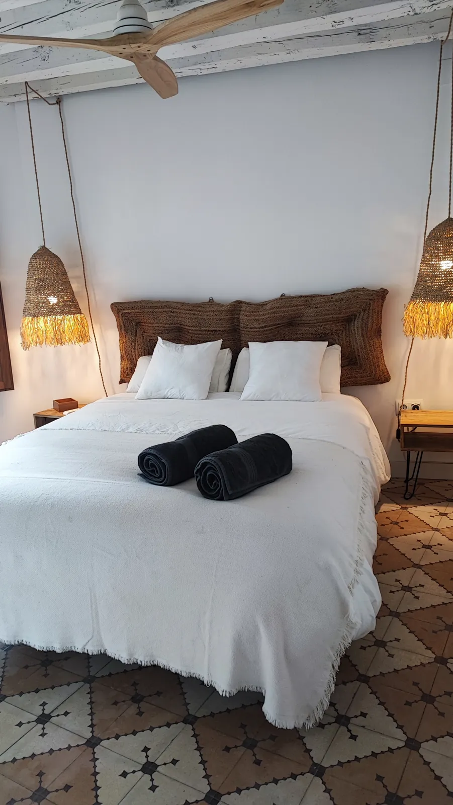 El dormitorio de Casa Chía con la cama vestida, lámparas de rafia y suelo de baldosa hidráulica
