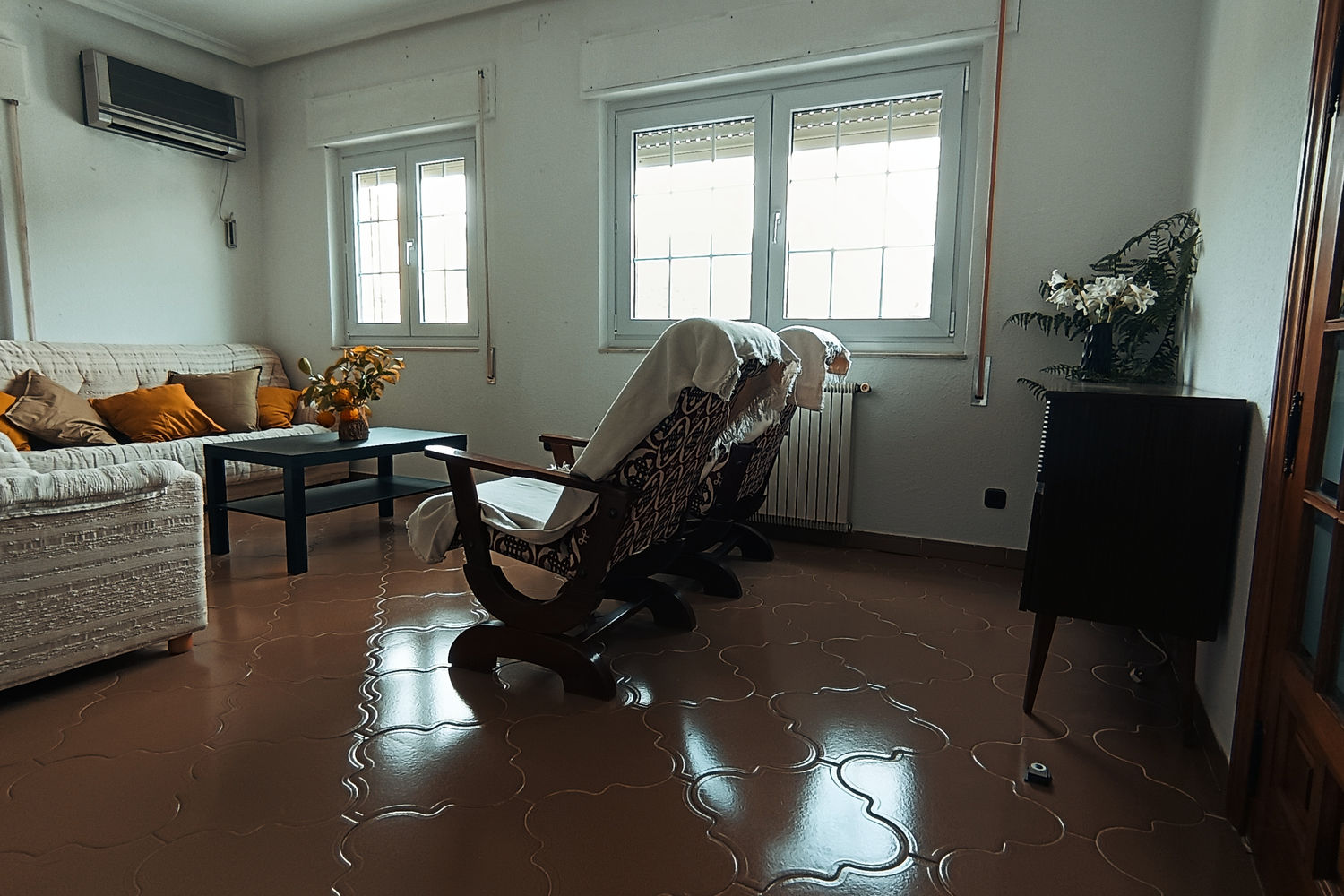 Salón de Villa Moiko con sofá amplio, mecedoras de madera y suelo de barro