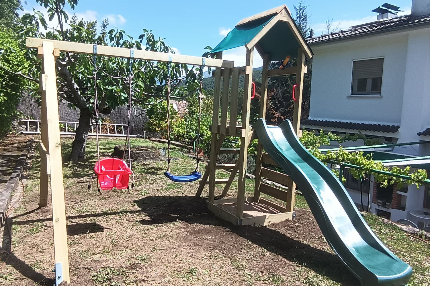 Jardín de Villa Moiko con parque infantil de madera, columpio y tobogán, junto a una higuera